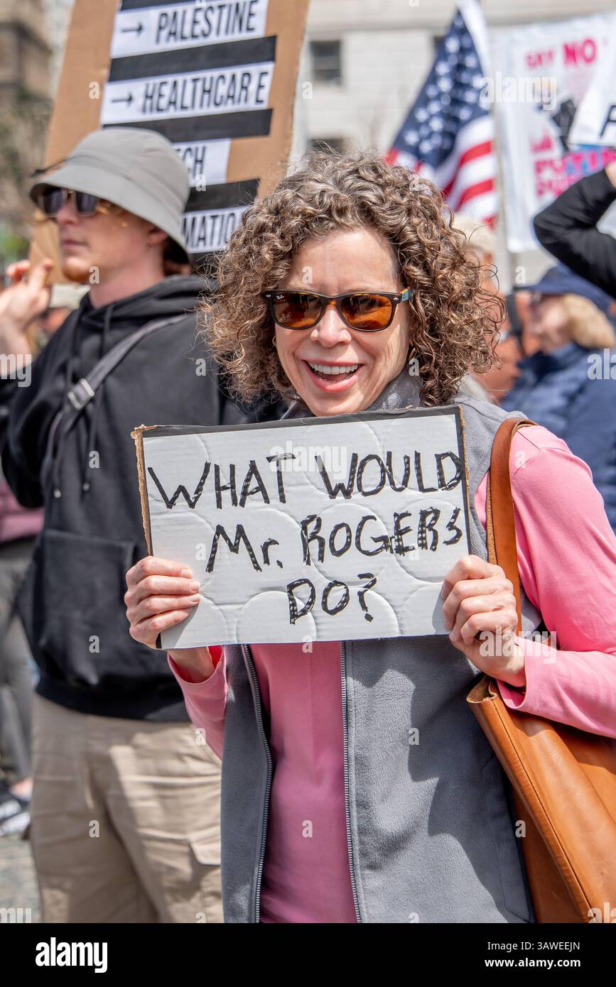 San Francisco, USA. 19th Apr 2025. At the Civic Center Plaza “Stop the Billionaire Agenda” protest against the Trump Administration, a woman smiles while displaying her sign reading, 'What would Mr. Rogers do?' Credit: Shelly Rivoli/Alamy Live News - Stock Image