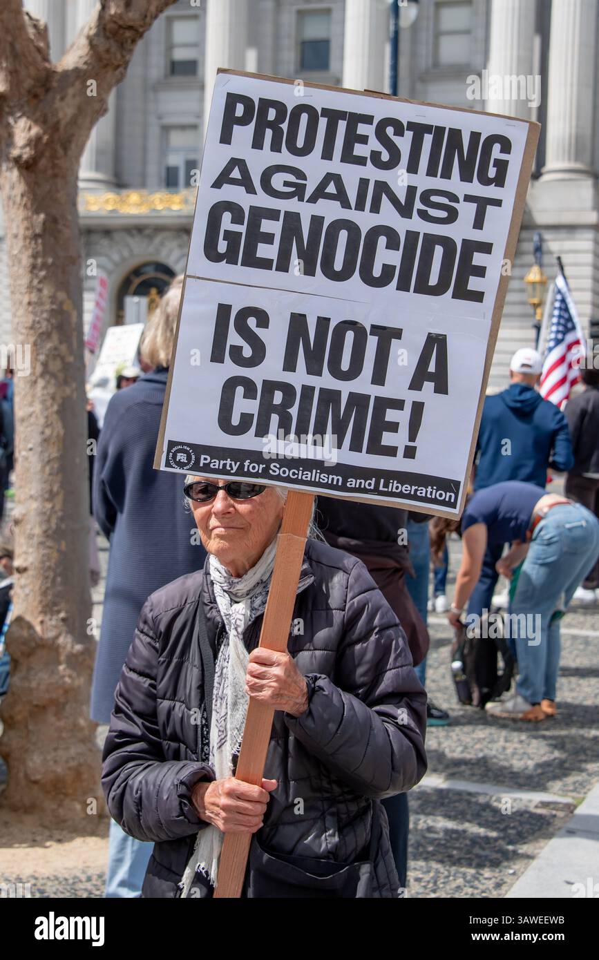 San Francisco, USA. 19th Apr 2025. At the Civic Center Plaza “Stop the Billionaire Agenda” protest against the Trump Administration, a woman carries a sign reading, 'Protesting against genocide is not a crime!'.    Credit: Shelly Rivoli/Alamy Live News - Stock Image