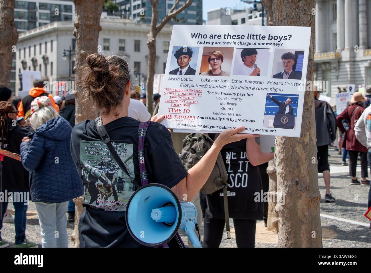 San Francisco, USA. 19th Apr 2025. At the “Stop the Billionaire Agenda” protest against the Trump Administration, a woman stands among the crowd with a megaphone at her side and sign reading, 'Who are these little boys? And why are they in  charge of our money?' which shows the young men Trump and Elon Musk hired as part of the DOGE Team. Credit: Shelly Rivoli/Alamy Live News - Stock Image