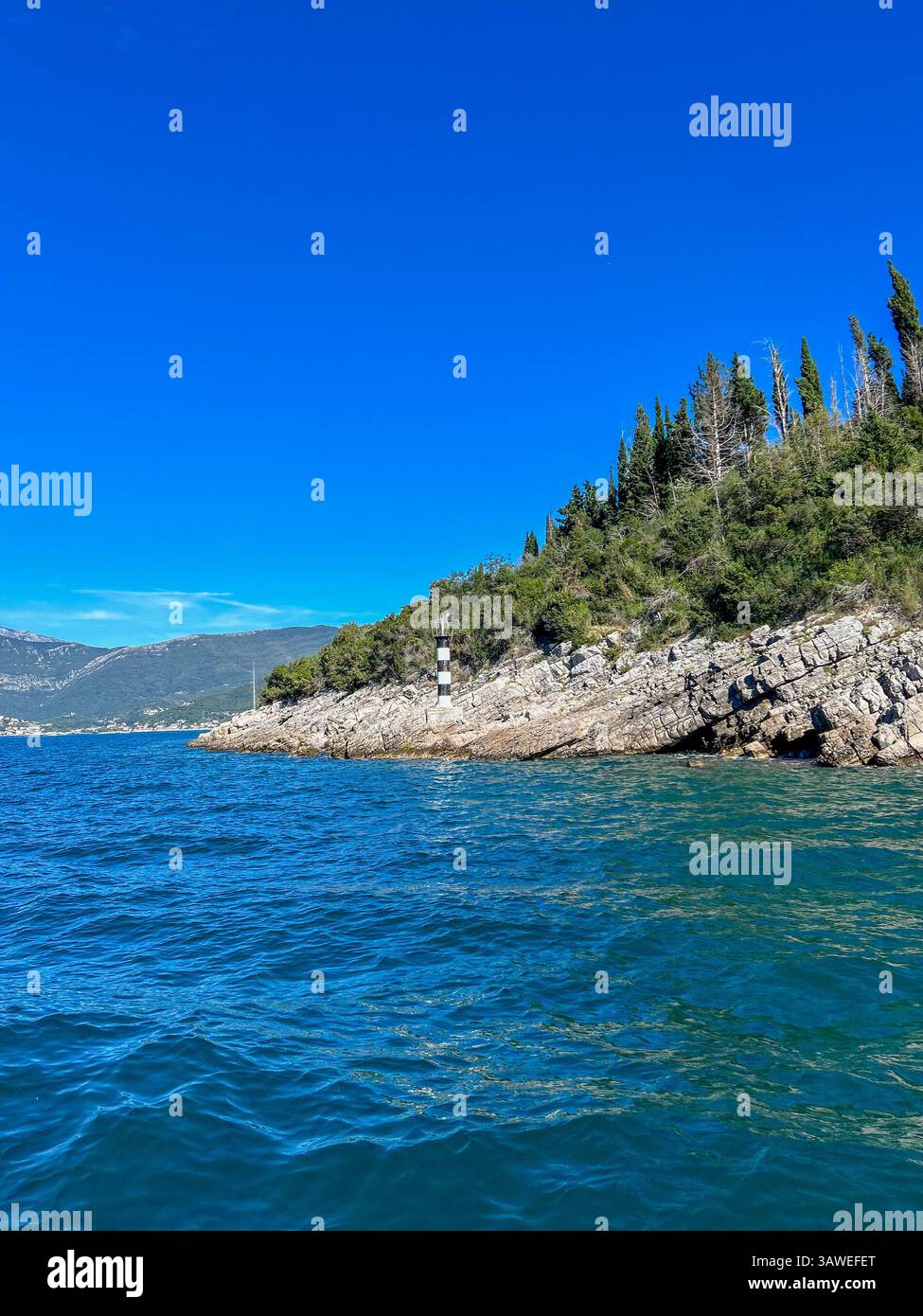 Lighthouse perched on a rocky ridge by the vivid blue waters at the Bay of Kotor's entrance. - Smartphone Captured Stock Image