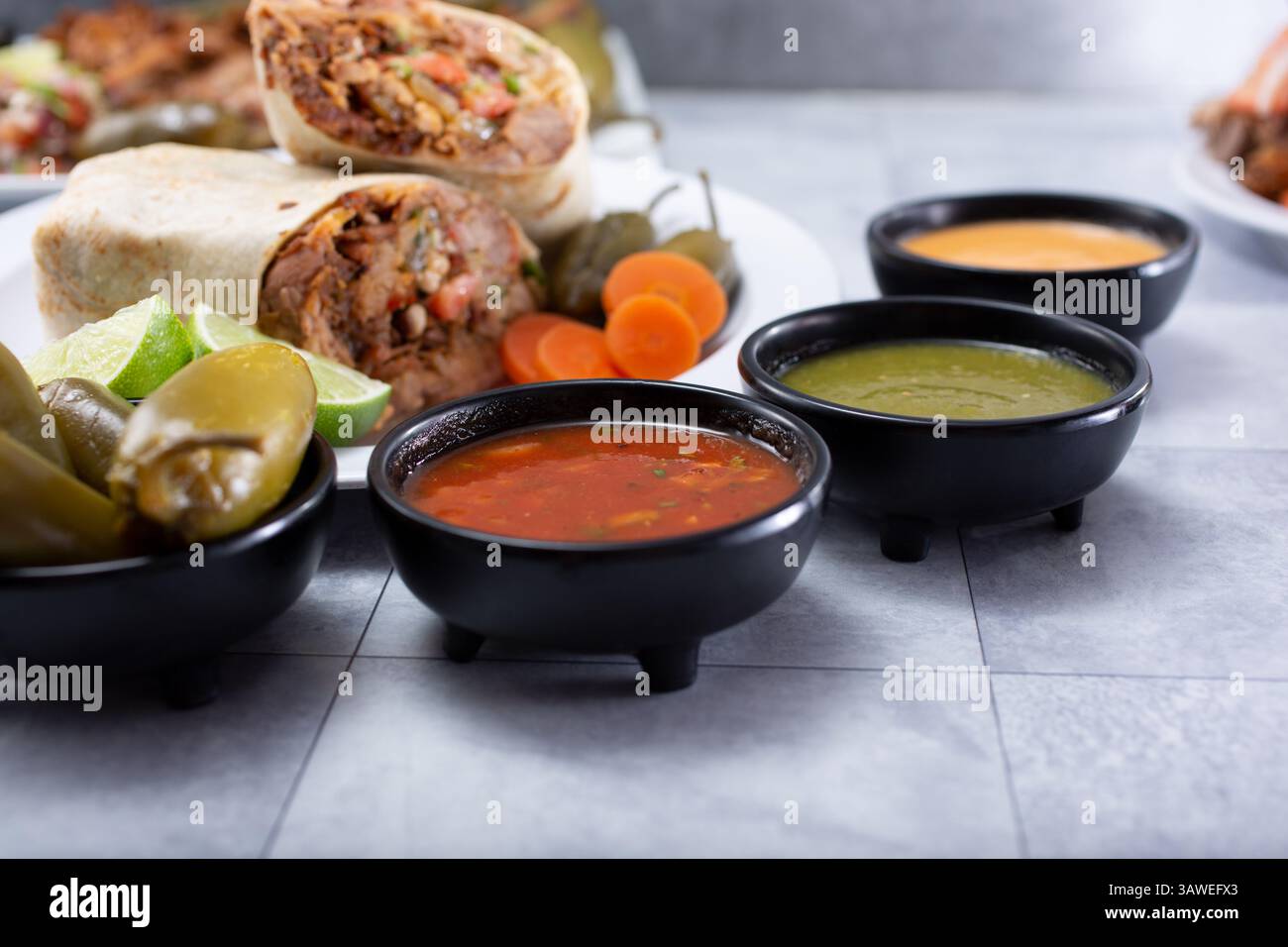 A view of several condiment cups of salsa, next to some Mexican entrees. Stock Photo