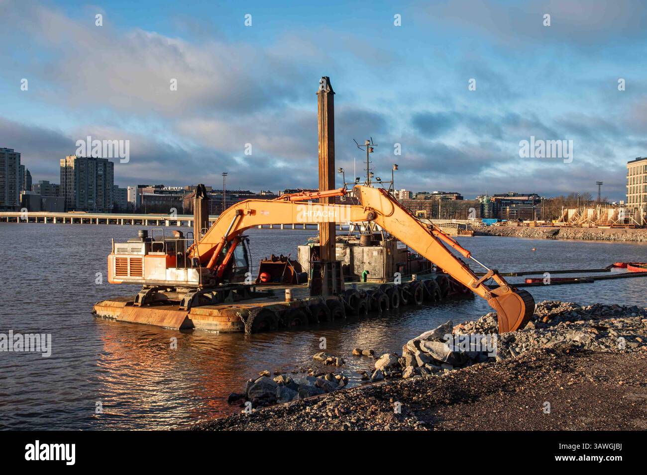 Pile-driving barge with Hitachi excavator in Nihti or Sompasaari district of Helsinki, Finland. Setting afternoon sun is coloring the landscape. Stock Photo
