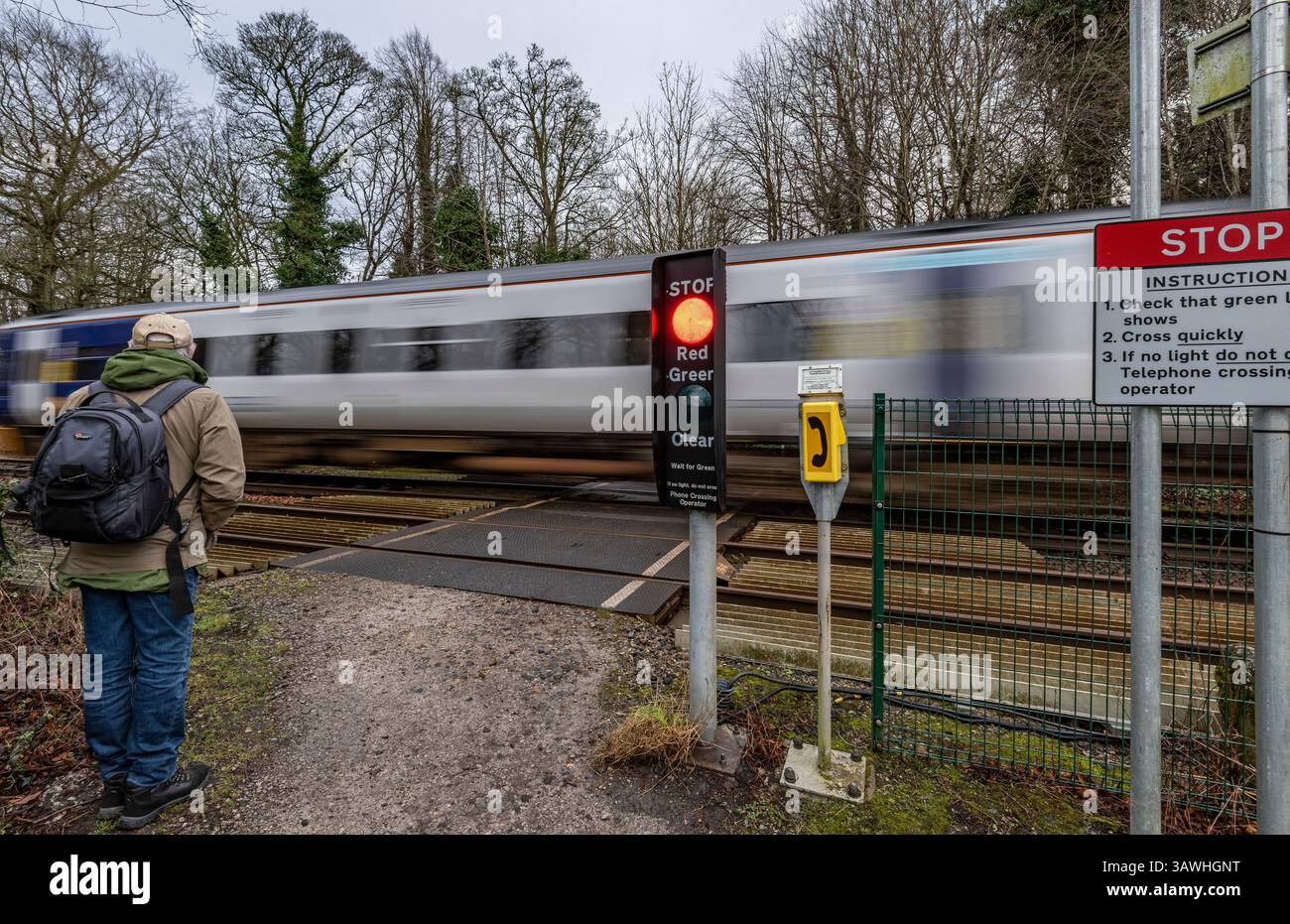 Pedestrian railway level crossing controlled by lights in rural environment with elderly man waiting as blurred speeding train passes Stock Photo