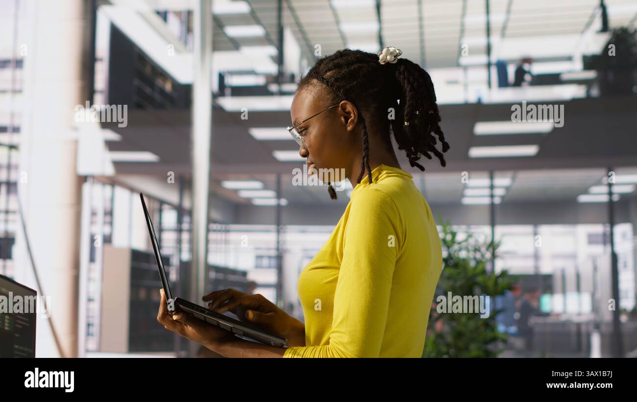 Computer scientist working, doing software debugging using notebook, troubleshooting errors. Woman standing in office, fixing coding issues using laptop, solving tasks, camera A Stock Photo