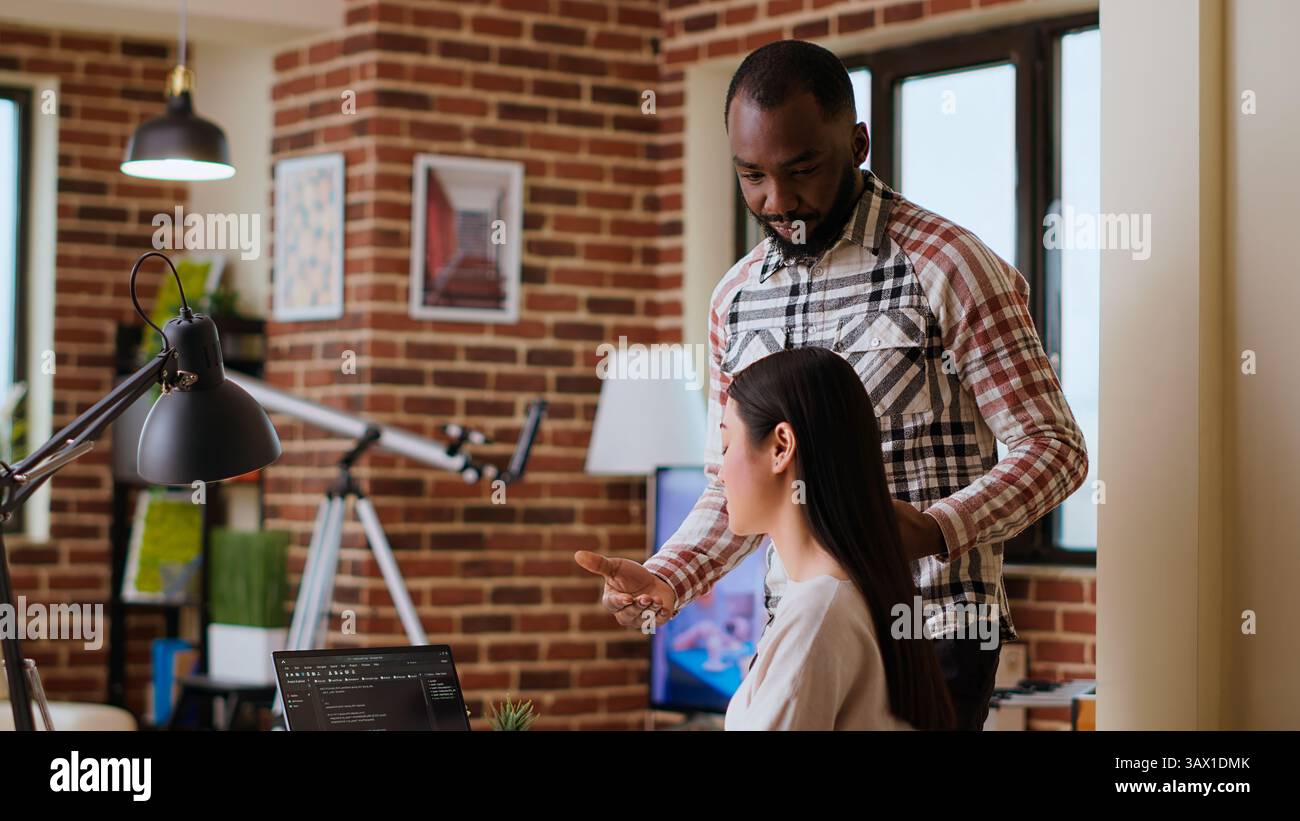 Diverse software developers team coding on a laptop in a cozy home office, working on a new program or app development. Specialists in IT promote programming language and remote tech work. Camera B. Stock Photo