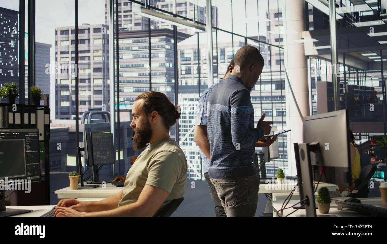 Managers evaluating work done by computer scientists in workspace doing software debugging. Management executives walking in office with tablet, checking code fixed by employees, camera B Stock Photo