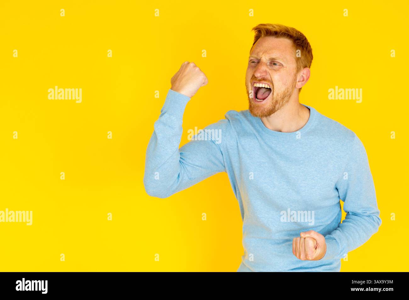 Excited man raising fists and shouting on yellow background Stock Photo