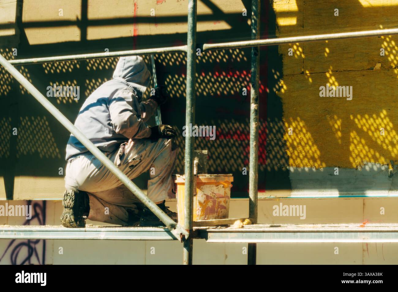 Construction worker on scaffolding working on building facade thermal insulation, selective focus Stock Photo