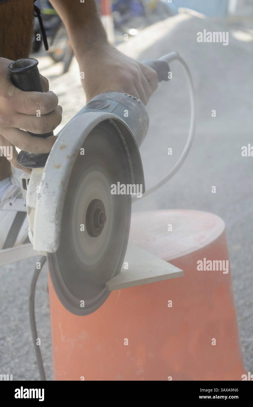 Skilled worker cuts tiles with angle grinder under dust exposure Stock Photo