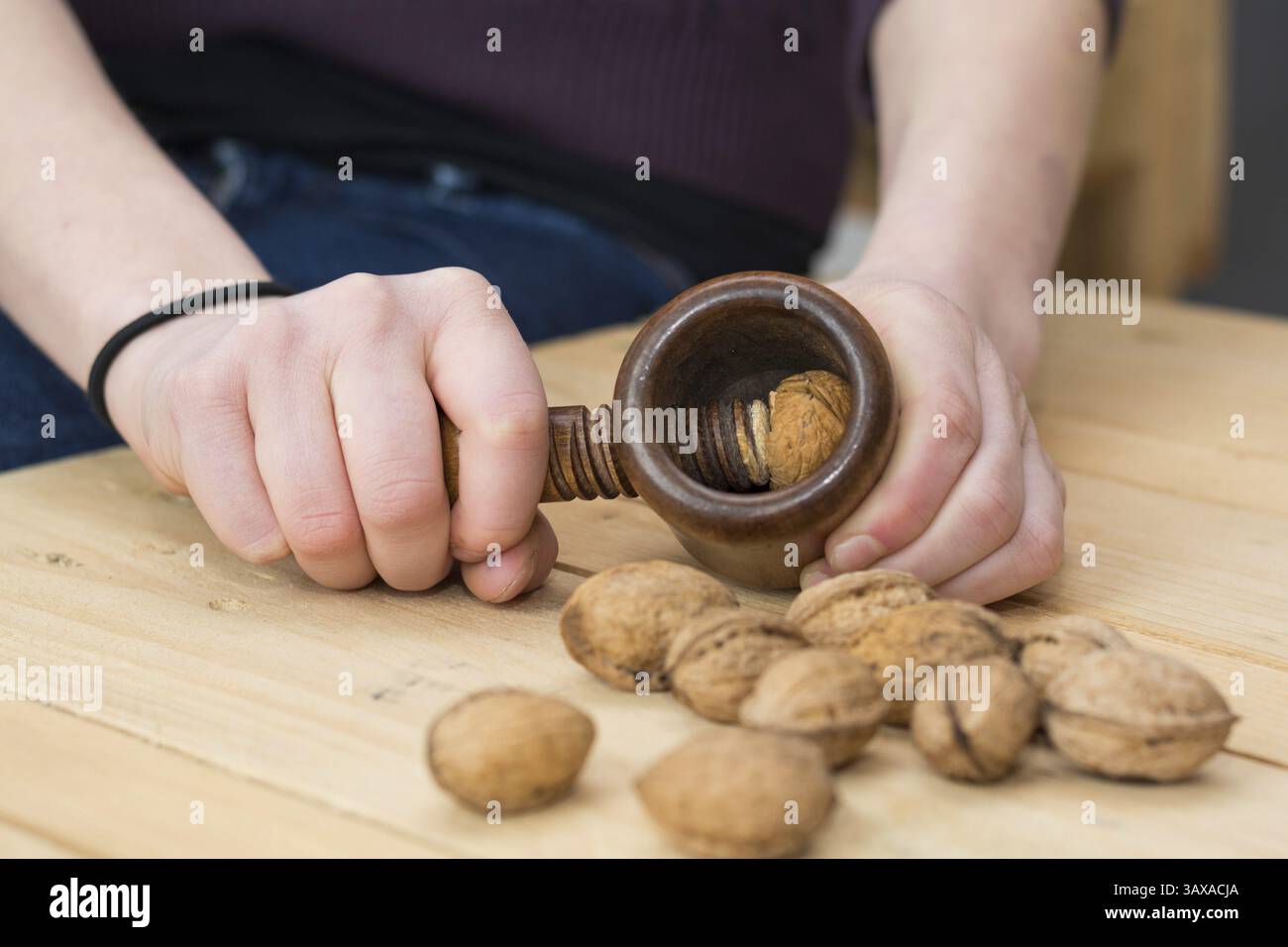 Person cracking walnuts on a rustic wooden table with a nostalgic nutcracker Stock Photo