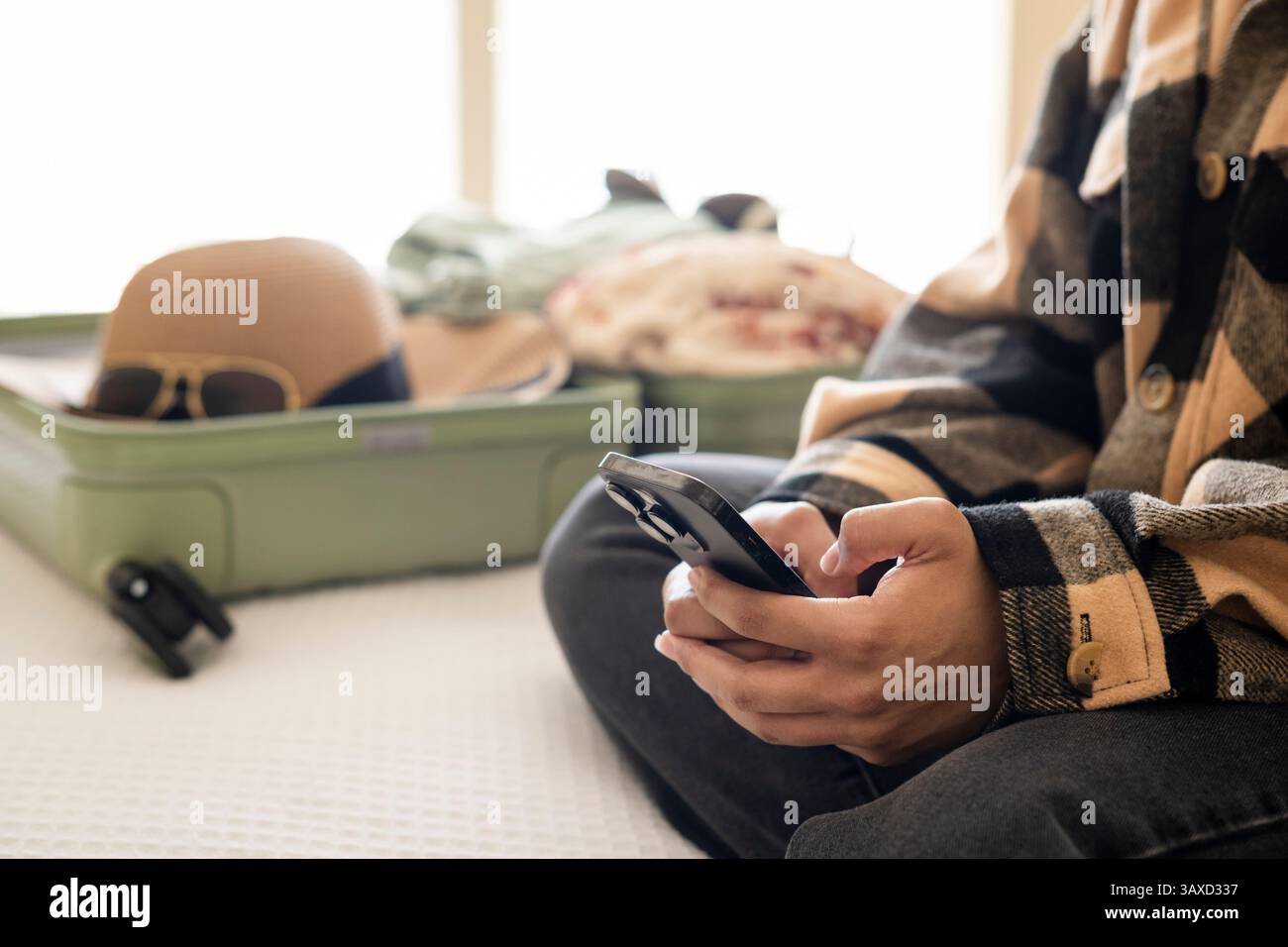 Hands holding phone with packed suitcase in background on bed Stock Photo