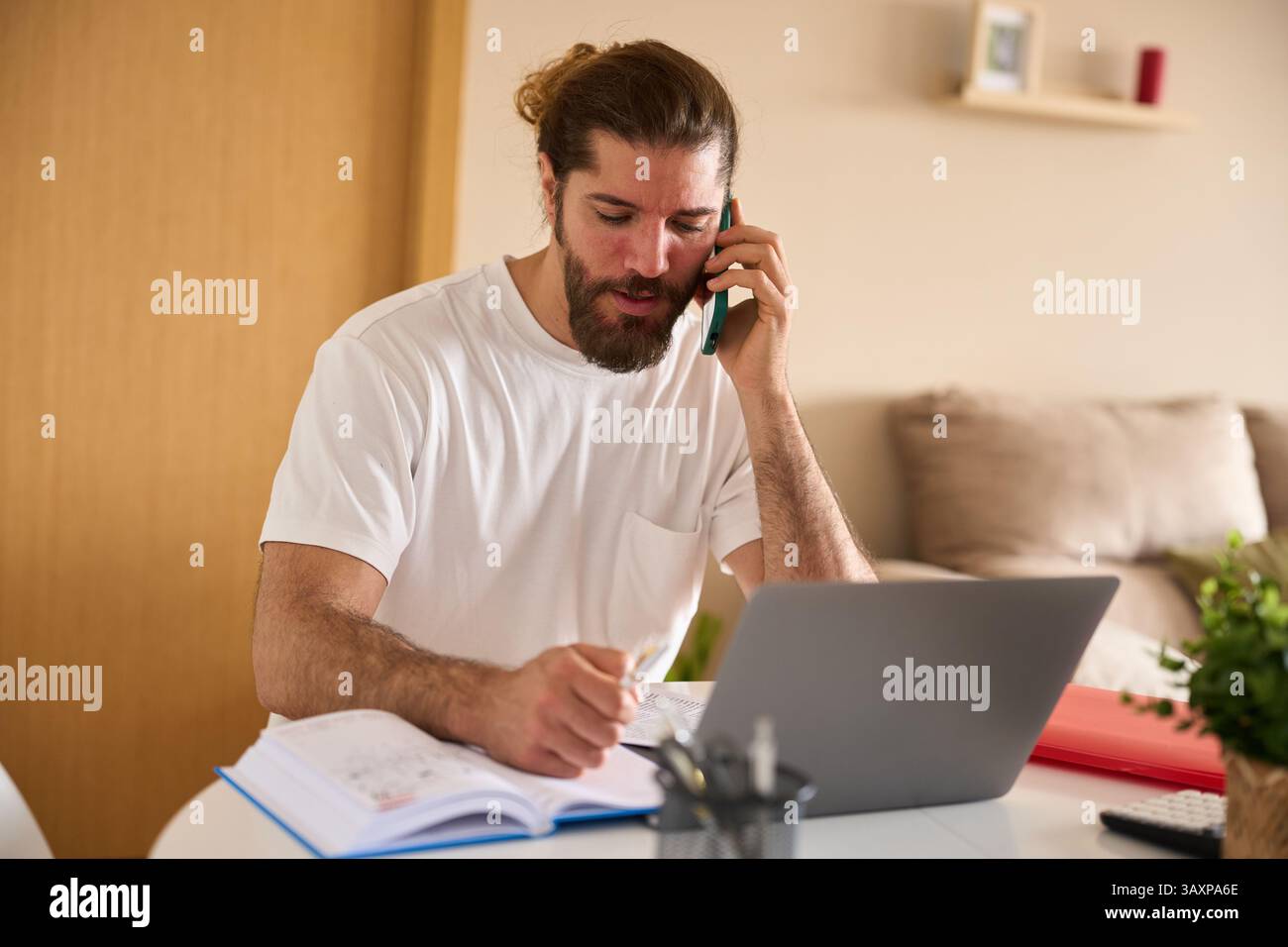 Freelancer working from home talking on phone and taking notes Stock Photo