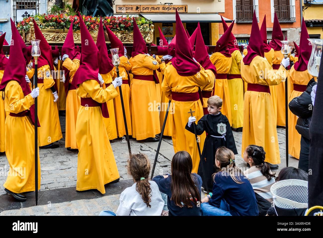 Good Friday procession En el Calvario in Cuenca. Procession in Spain with participants in golden yellow and wine-red robes. A boy carries a cross. Plaza Mayor, Cuenca, Castile-La Mancha, Spain Stock Photo