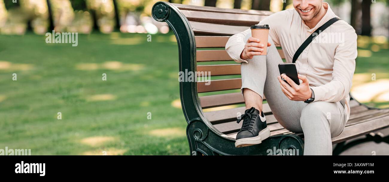 Young man enjoying coffee while using smartphone in urban park setting Stock Photo