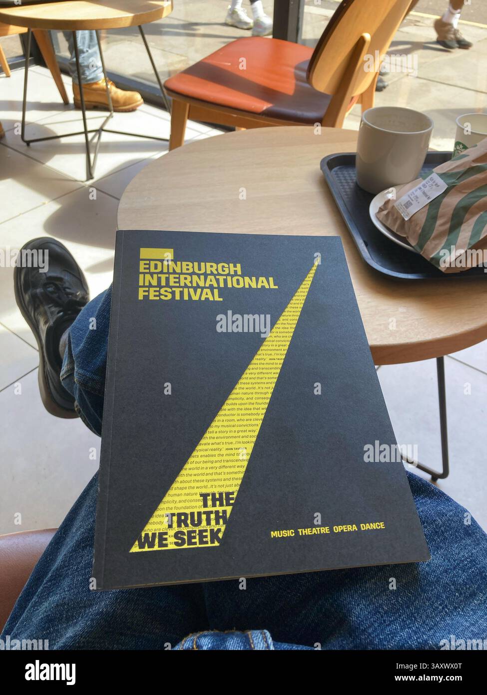 Browsing the Edinburgh International Festival programme in the cafe, paper copy for 2025, the festival dates are 1st–24th August 2025 - Smartphone Captured Stock Image