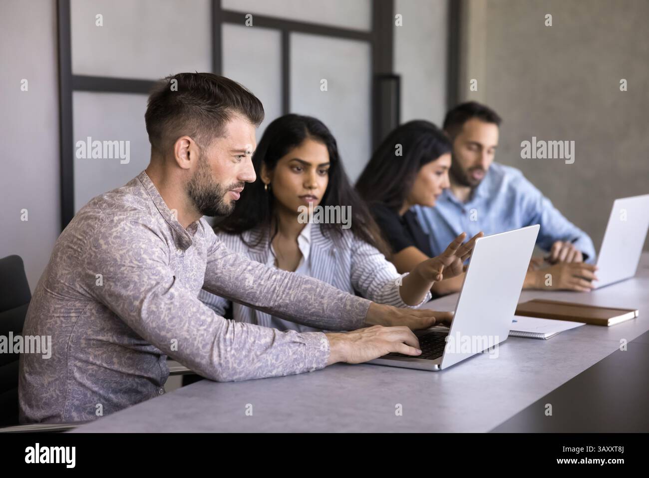 Two multinational workmates using laptop, working on joint tasks Stock Photo