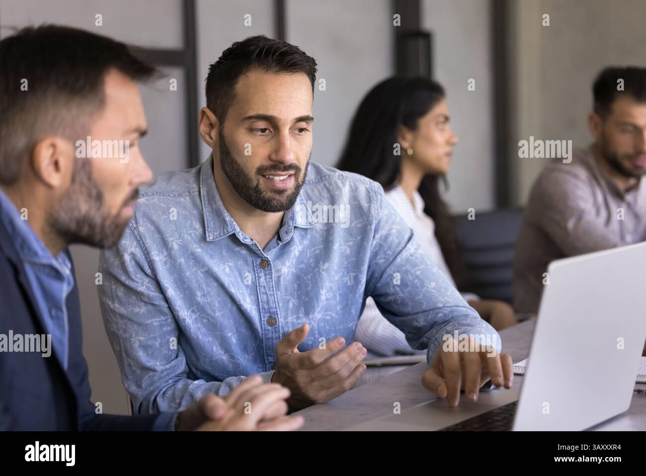 Two colleagues sit at desk working together using laptop Stock Photo