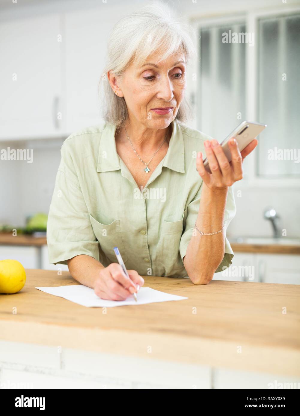 Elderly woman using phone and writing notes Stock Photo