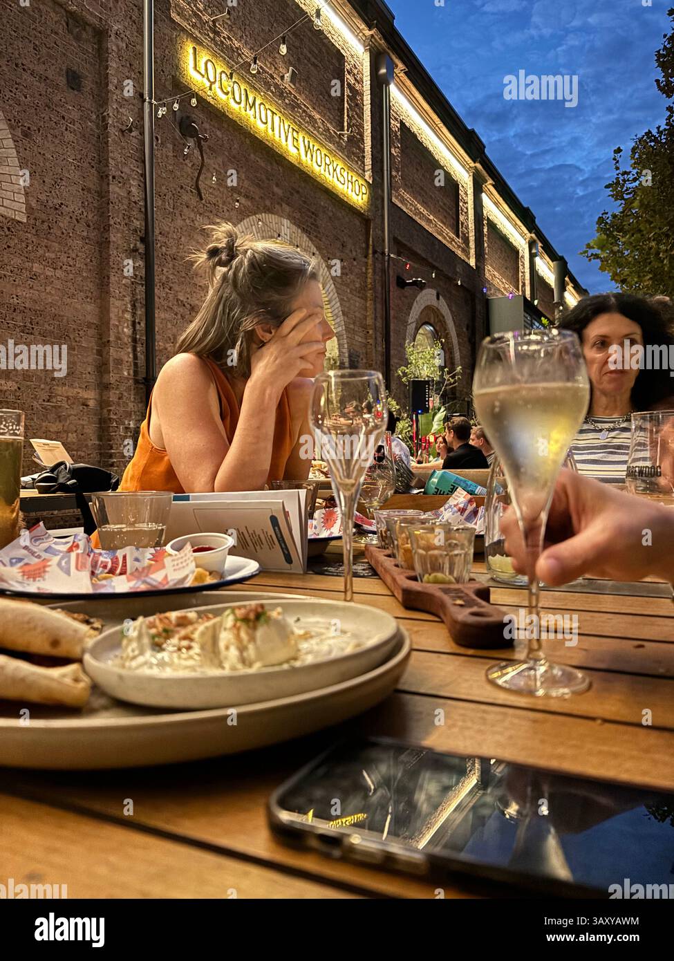 Women drinking and eating outdoors at Brewdog, Locomotive Workshop, South Eveleigh, Redfern, Sydney, NSW, Australia. no MR or PR - Smartphone Captured Stock Image