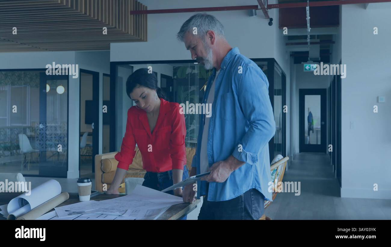 Two architects are collaborating over plans in flat architecture office, with tubes and coffee Stock Photo