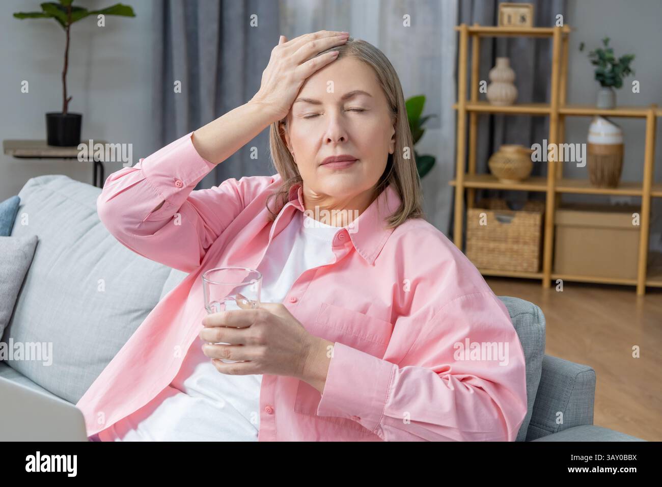 Feeling unwell. Woman sitting on the sofa and taking pills from a headache Stock Photo