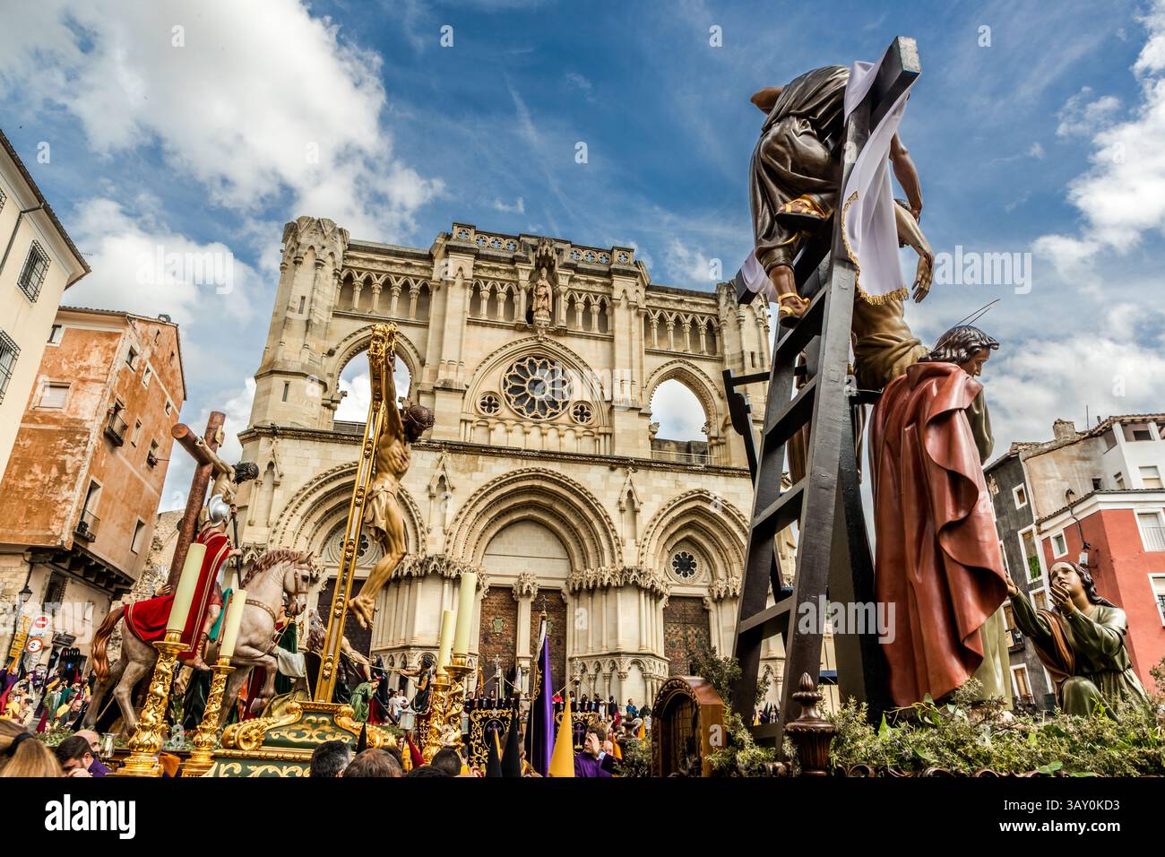 Several pasos of the Good Friday procession Camino del Calvario stand in front of Cuenca Cathedral, Castilla-La Mancha, Spain: a mounted figure, a cross and a figure of Christ on a tall ladder. Construction of the Cathedral of Santa María y San Julián began in 1182 and it was consecrated in 1208, making it, in its French-influenced Gothic style, one of the country's earliest Gothic buildings. Its present façade was rebuilt in neo-Gothic style after a partial collapse in 1902. During Semana Santa in Cuenca, 33 Hermandades take part in eleven processions through the city during Holy Week. Stock Photo