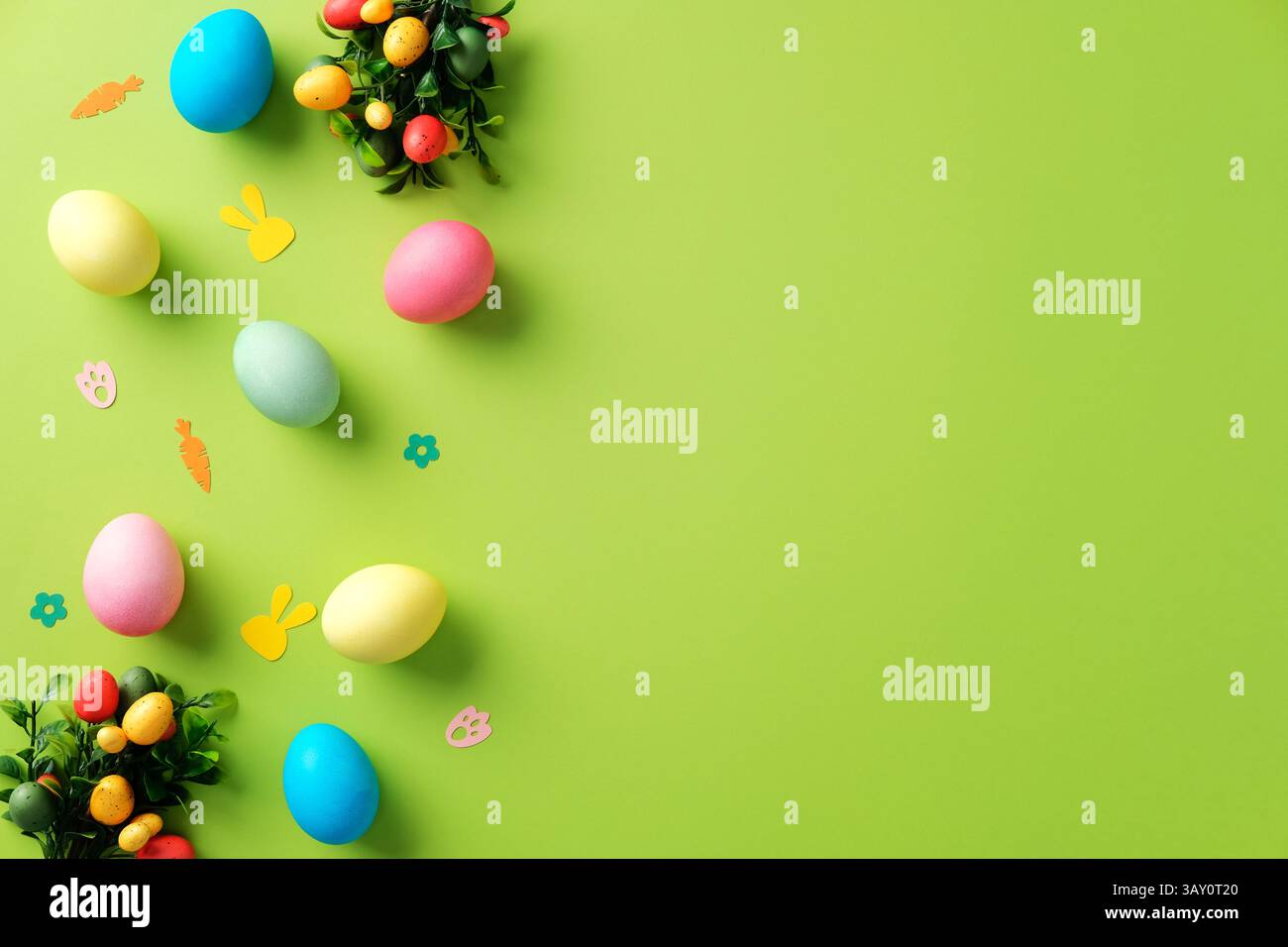 Happy Easter background with colorful Easter eggs and confetti on bright green table. Stock Photo