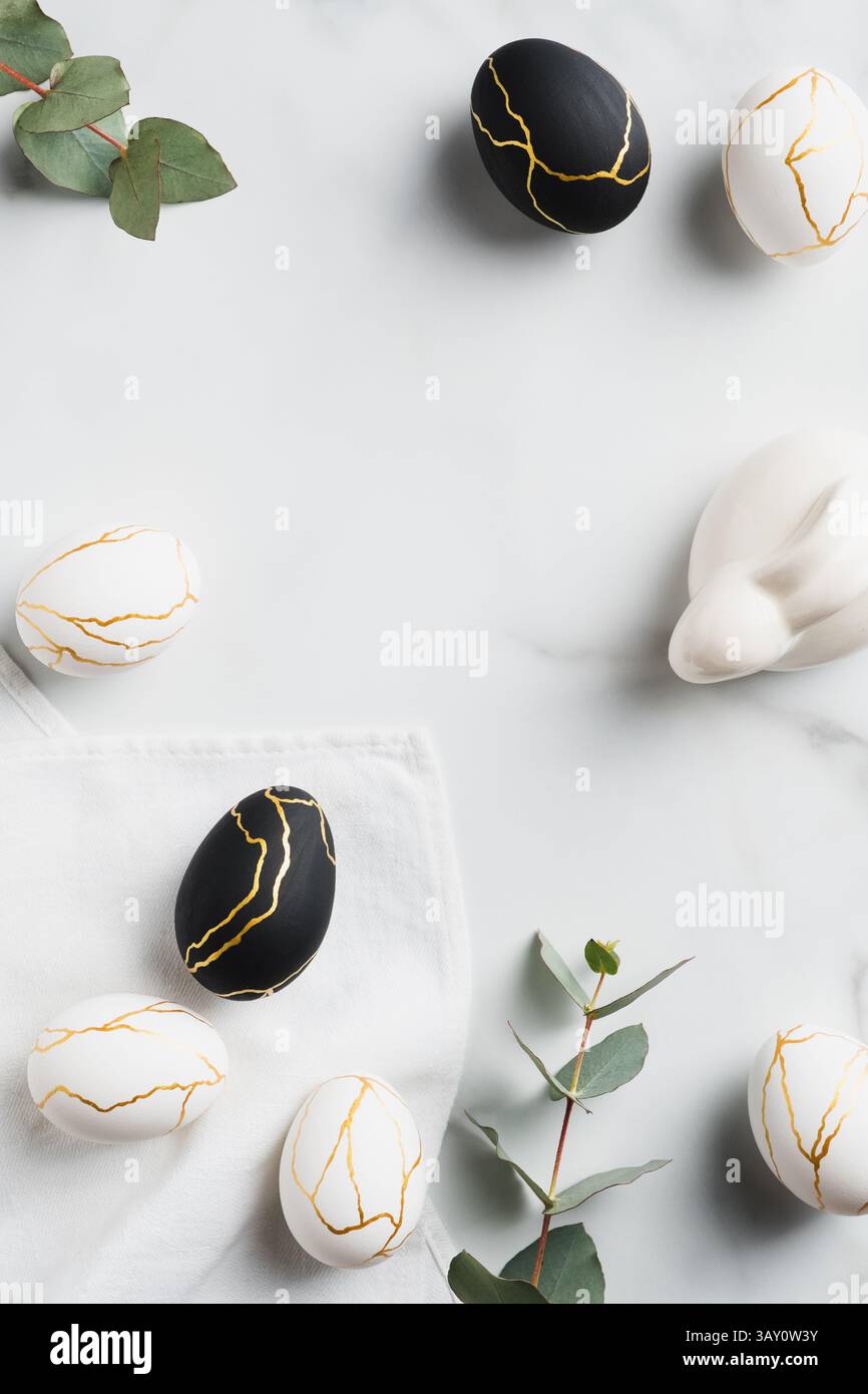 Elegant Easter flat lay composition. Luxury Easter eggs decorated gold, Easter bunny rabbit, eucalyptus on marble table. Top view. Stock Photo