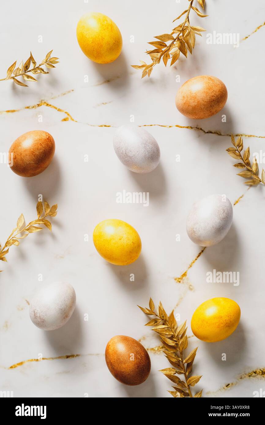 Happy Easter flat lay composition. Easter eggs and golden leaves on marble table top view. Stock Photo