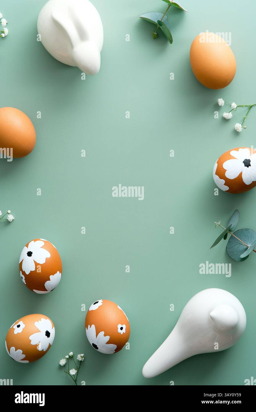 Easter flat lay vertical composition. Easter eggs, flowers, Easter bunny on pastel green background. Stock Photo