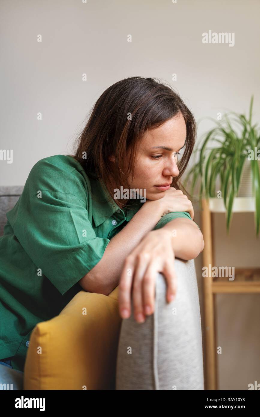 Sad and tired woman sitting on sofa at home looking down Stock Photo