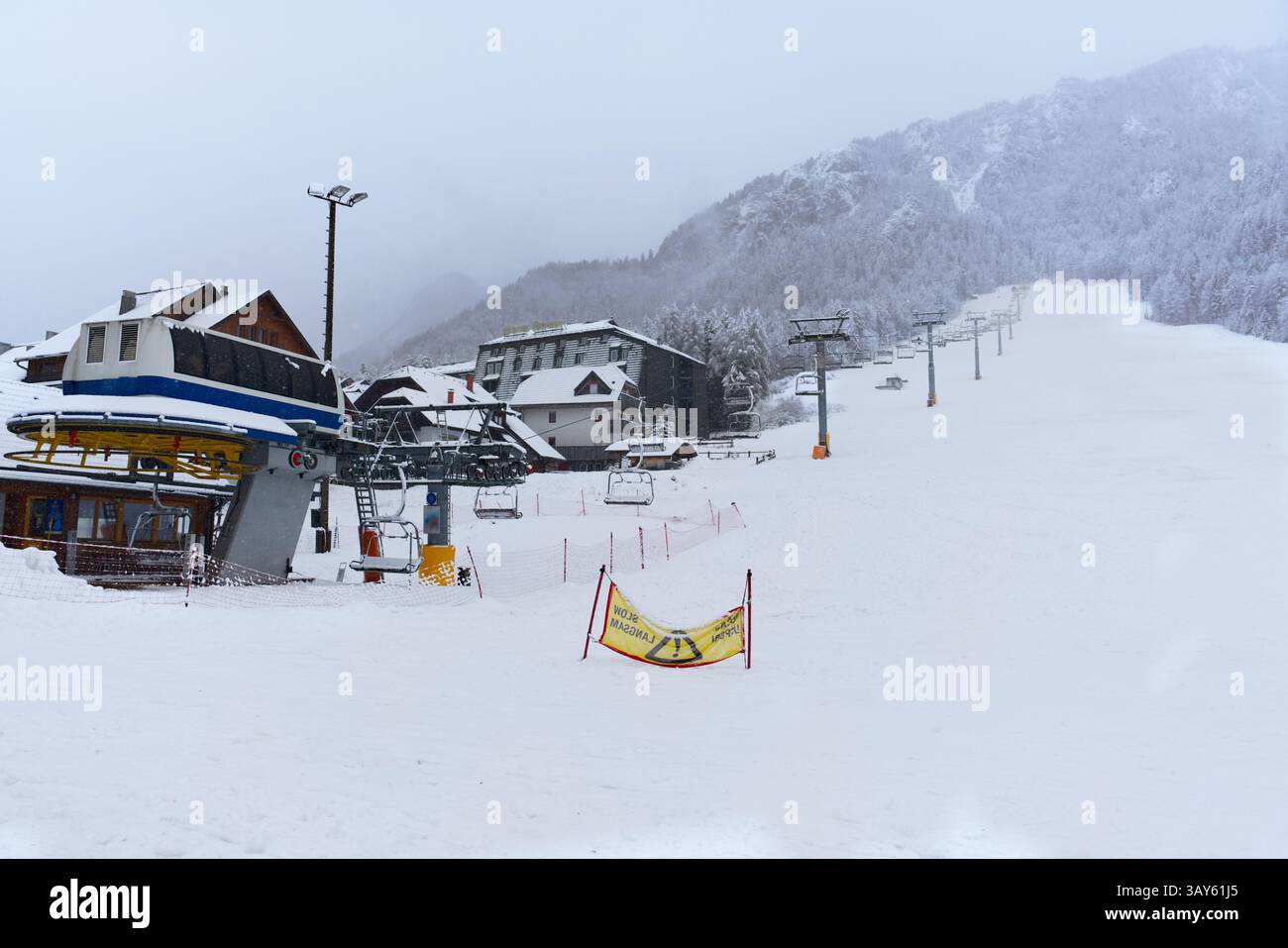 A snowy ski slope stretches through a wintery forest, with skiers descending amidst snow-covered trees and lift infrastructure Stock Photo
