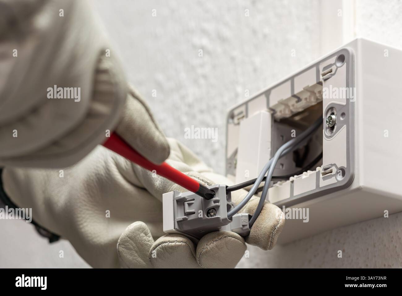 Electrician worker with screwdriver fixes electrical wires in the terminals of the diverter switch of an electrical system. Working safely with protec Stock Photo
