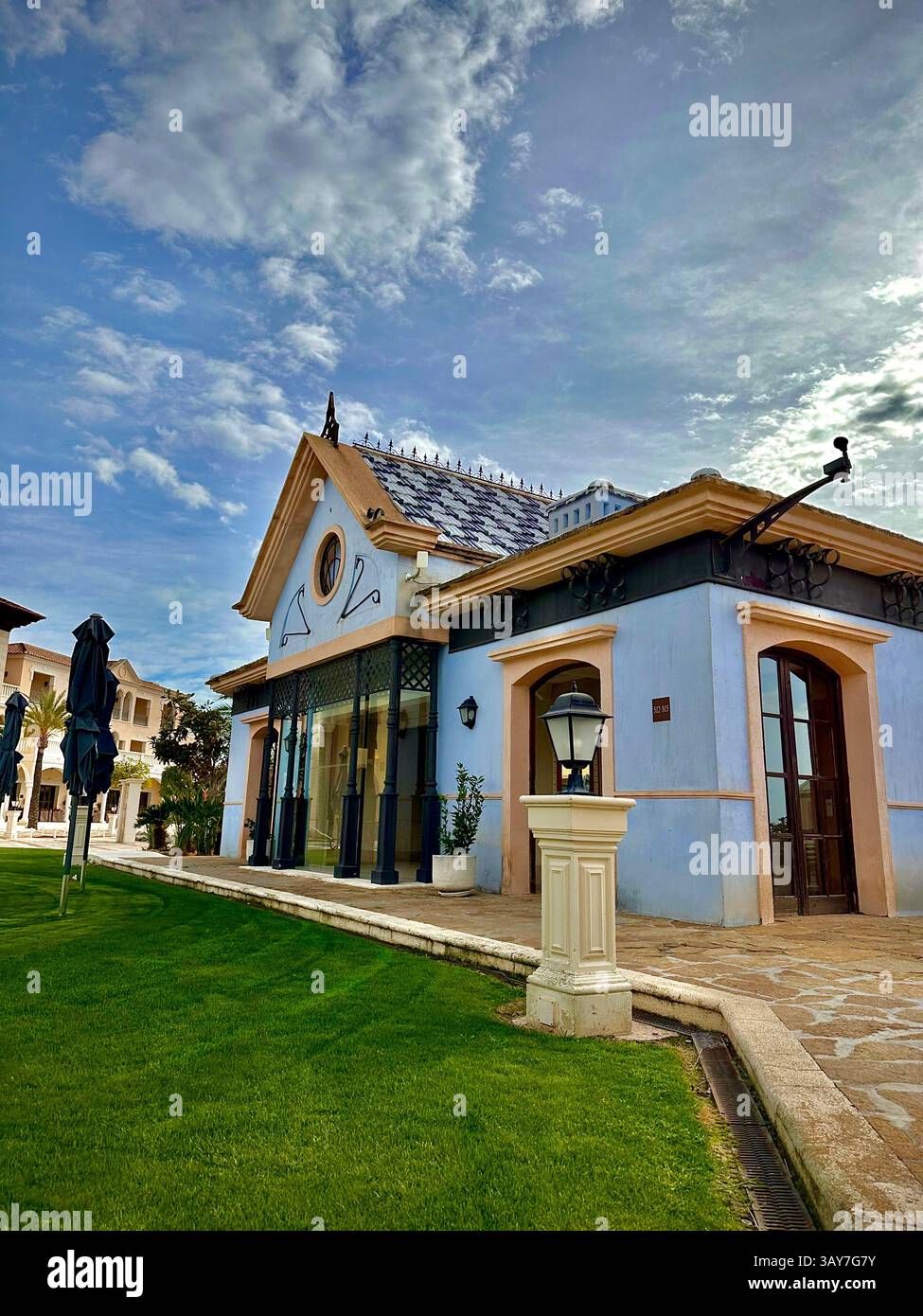 This image features the elegant facade of a European-style villa framed by a well-maintained garden with dense greenery and manicured bushes. The soft - Smartphone Captured Stock Image