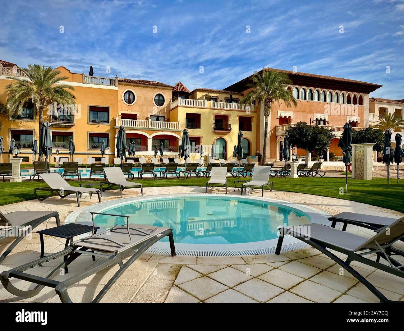 This image captures a tranquil Mediterranean poolside area featuring beige stone tiles, elegant lounge chairs, and soft palm tree shadows on a sunny a - Smartphone Captured Stock Image