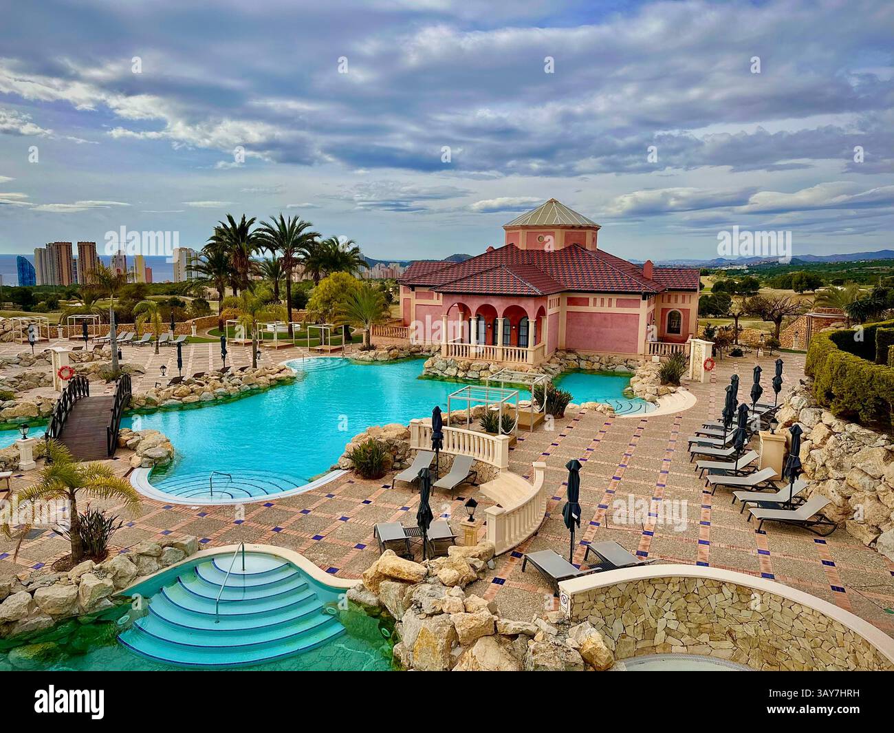This image shows a peaceful resort pool reflecting nearby palm trees and surrounded by soft beige architectural elements. The warm sunlight enhances t - Smartphone Captured Stock Image