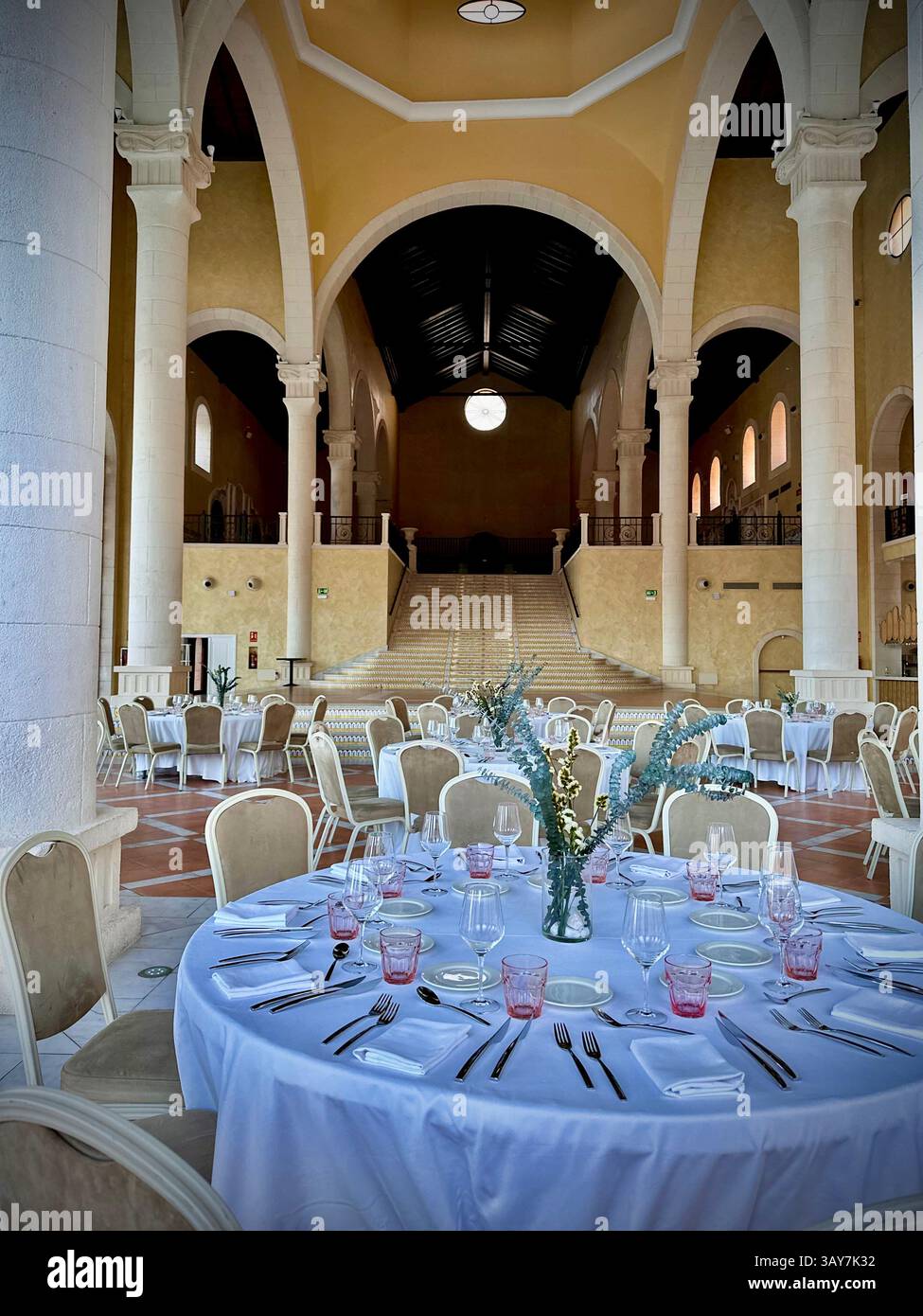 This photo captures a spacious dining hall featuring large stone arches, rustic textures, and natural light flooding through the open walls. The symme - Smartphone Captured Stock Image