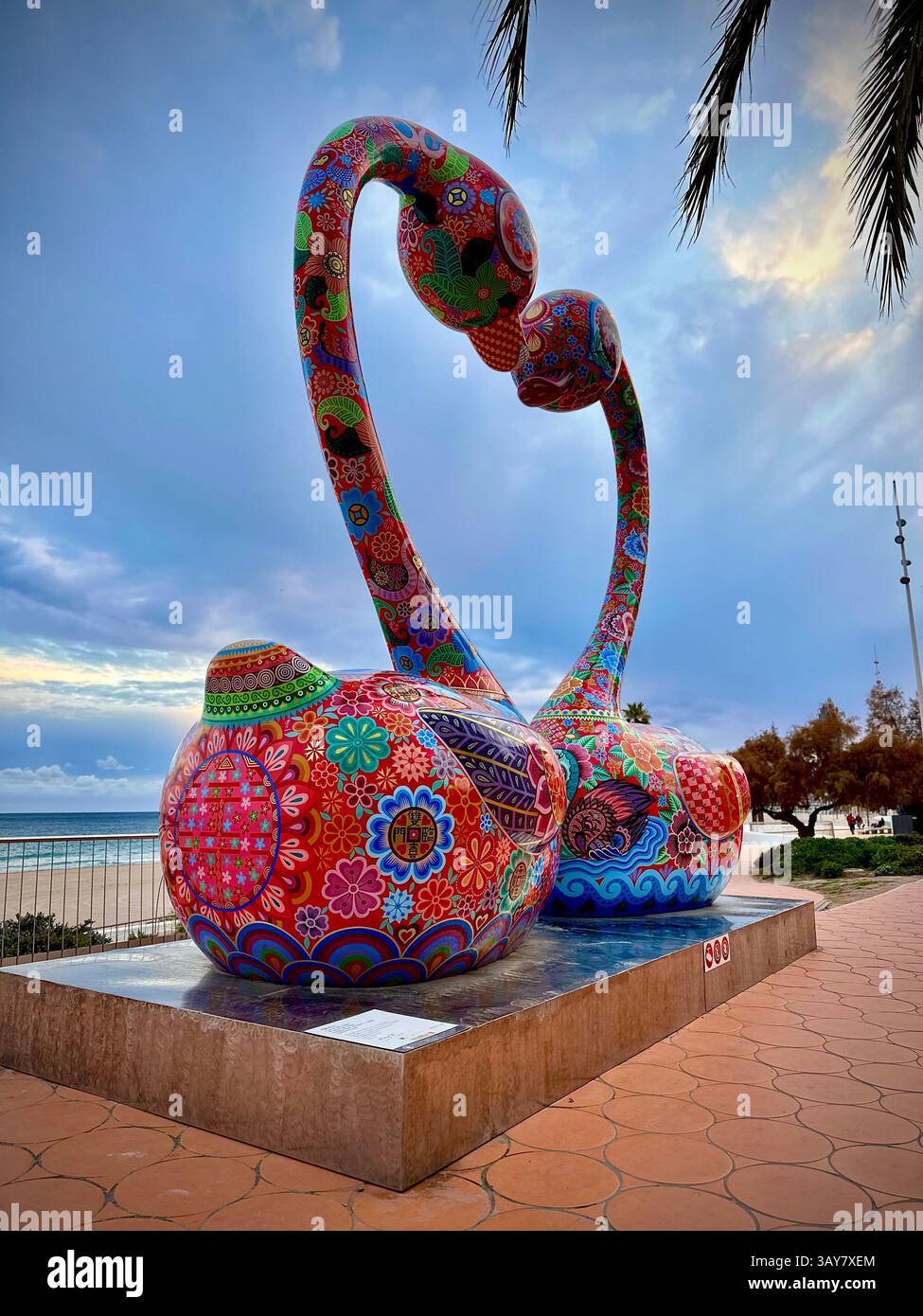 Two vibrant cat sculptures share a kiss under a dramatic sky. Painted with joyful patterns and bold colors, this artwork creates a playful and emotion - Smartphone Captured Stock Image