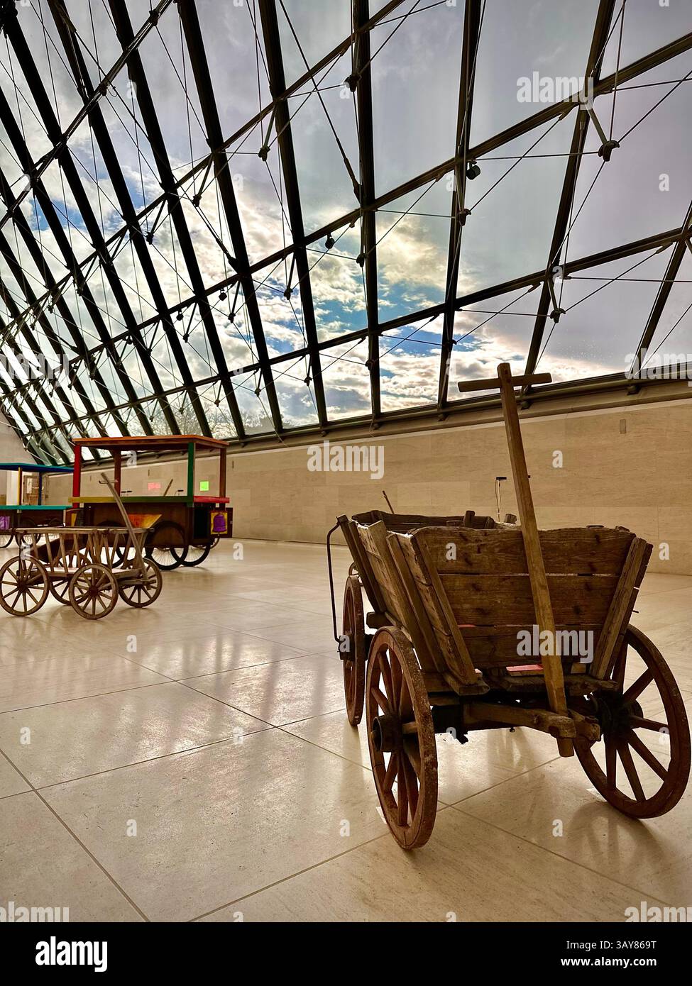 An exhibition of vintage wooden carts displayed under a stunning glass roof in a Luxembourg museum. The natural light and minimalistic space enhance t - Smartphone Captured Stock Image