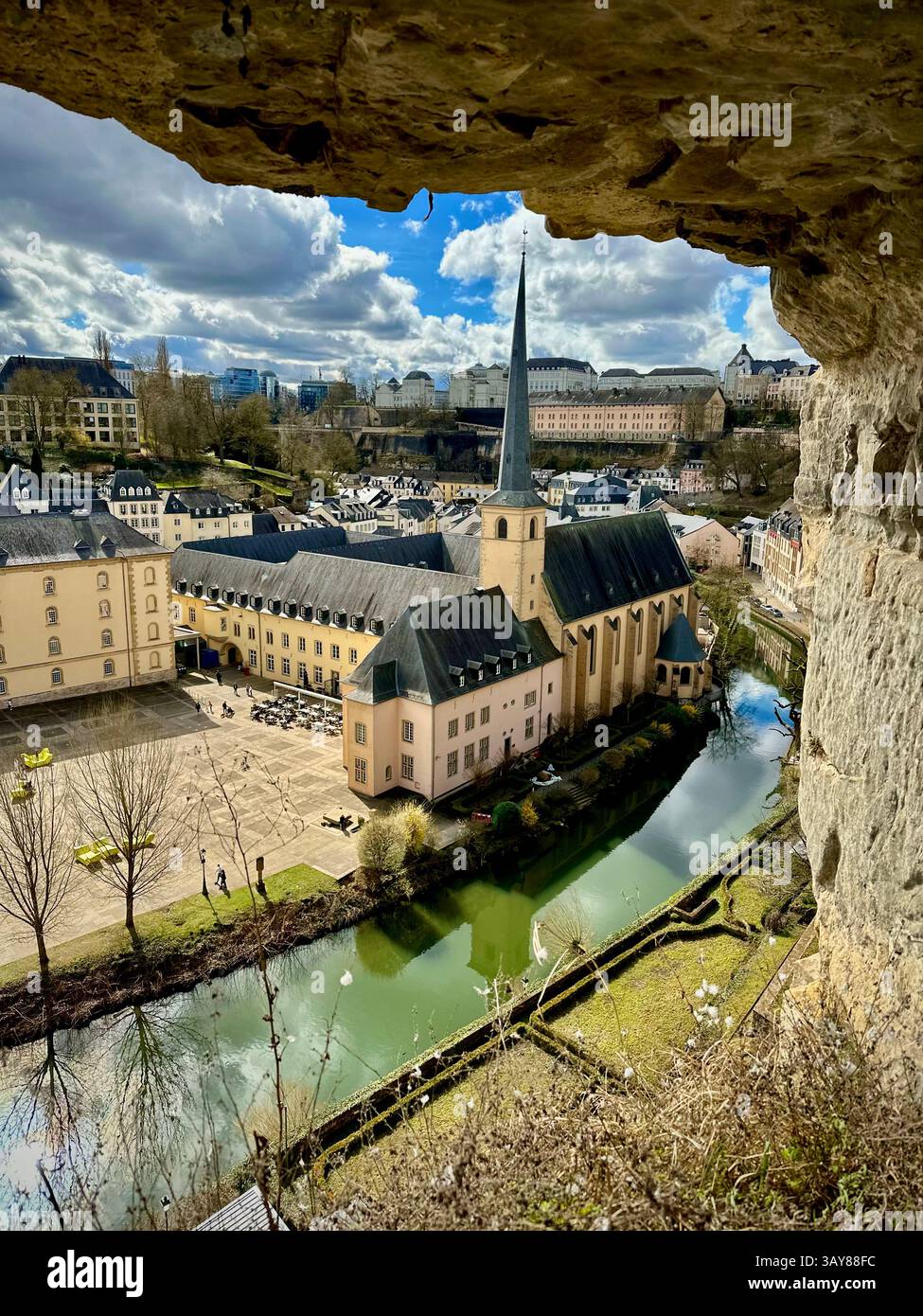 A scenic view of a historic church and a river in the old town of Luxembourg, taken from a rocky opening. The photo captures the peaceful charm of the - Smartphone Captured Stock Image