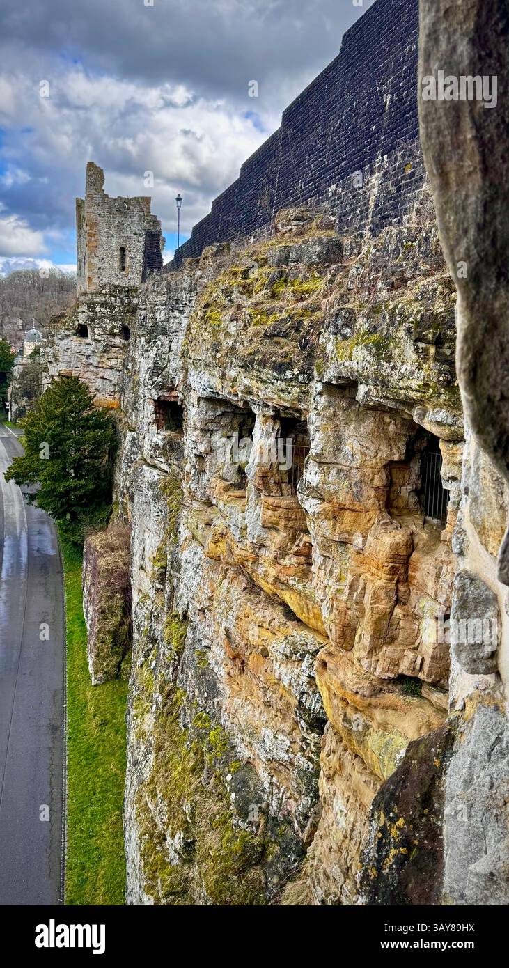 A close-up view of ancient rock fortifications in Luxembourg, featuring carved openings and moss-covered textures. The dramatic sky and historic atmos - Smartphone Captured Stock Image