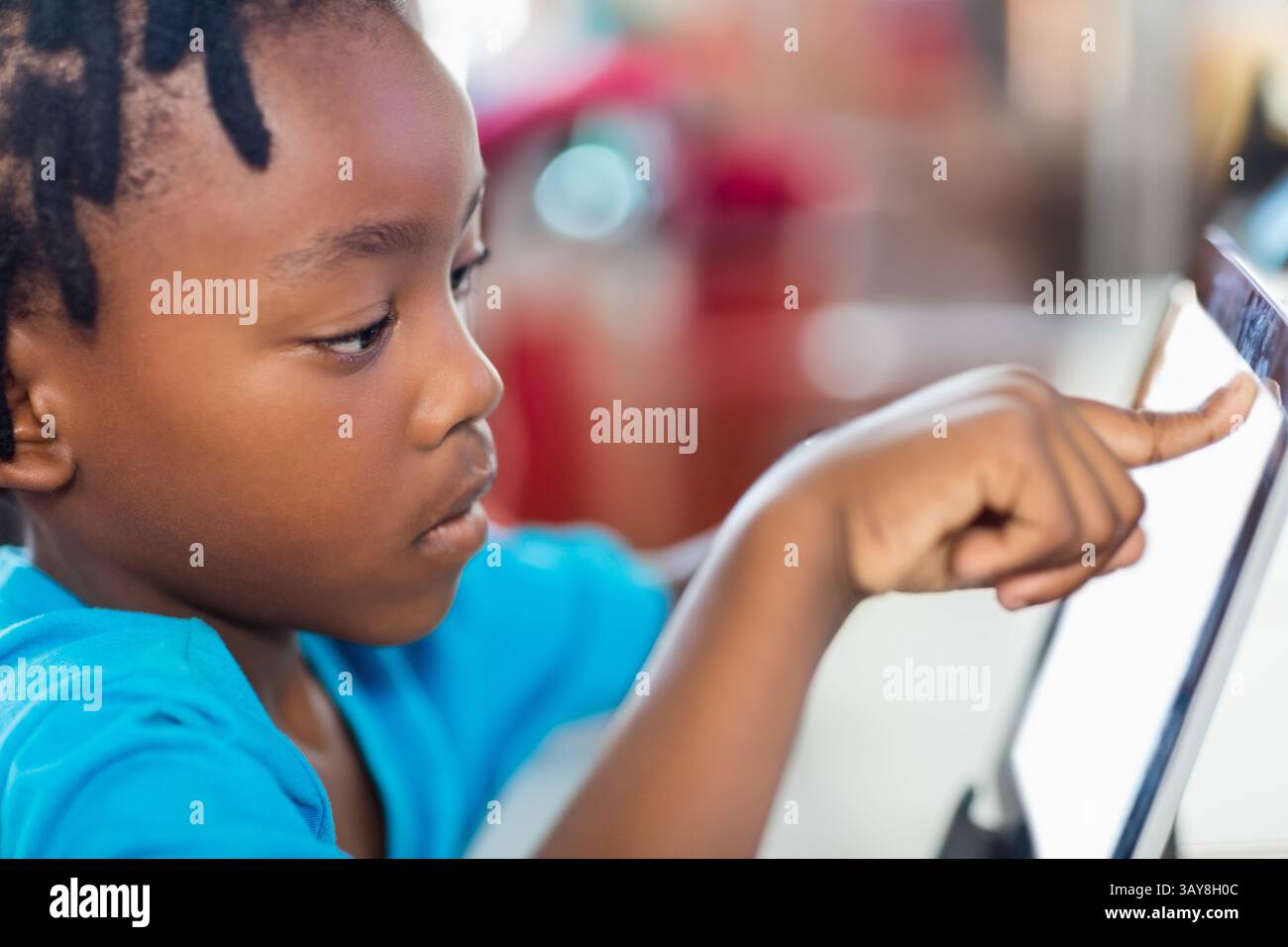 African American child leaning forward at table touching tablet on ...