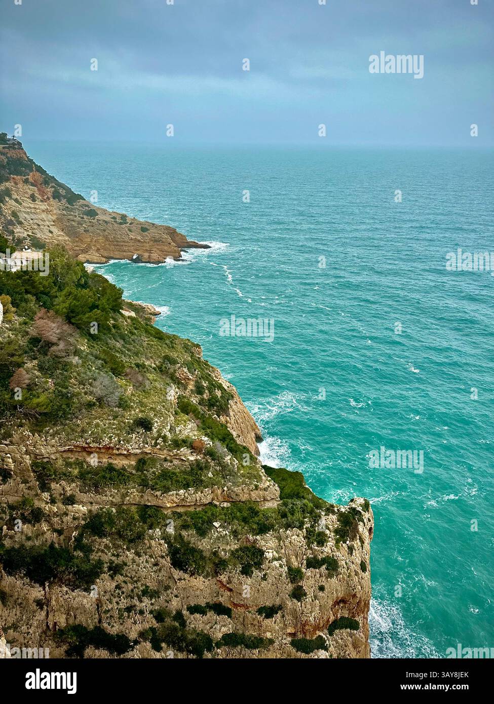 Majestic coastal cliffs with lush green vegetation overlooking a vibrant turquoise sea. Waves crash gently against the rocks under a cloudy sky, creat - Smartphone Captured Stock Image Majestic coastal cliffs with lush green vegetation overlooking a vibrant turquoise sea. Waves crash gently against the rocks under a cloudy sky, creat - Smartphone Captured Stock Image
