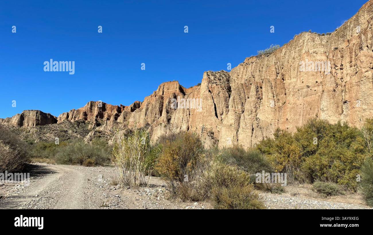 Steep sided eroded rocks in the Alpujarra, Andalucía, Spain with plants below and a blue sky. - Smartphone Captured Stock Image