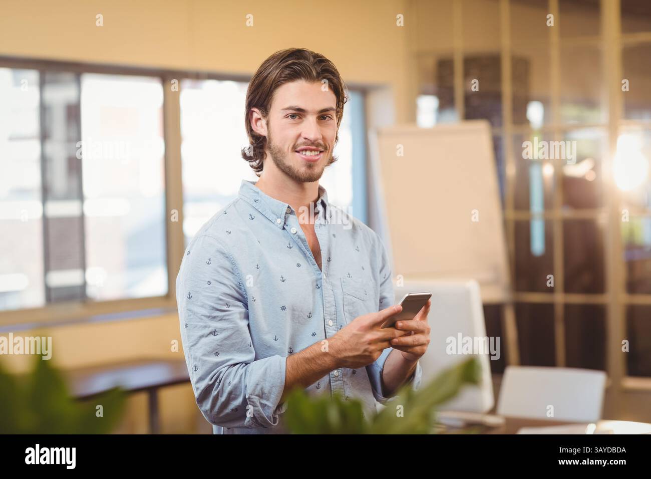 Man standing holding smartphone in office space, with flip chart and ...