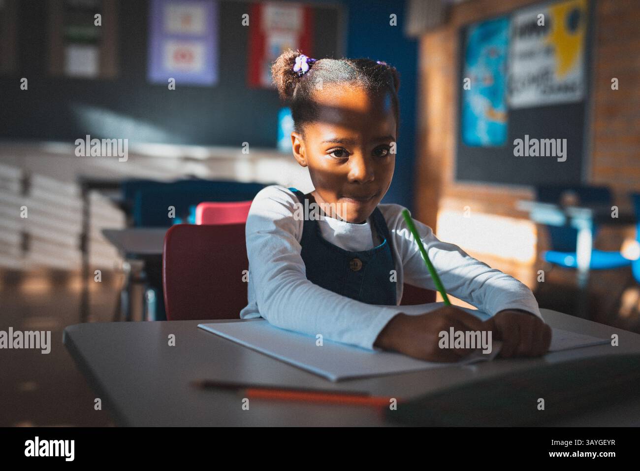 African American girl sitting at desk in school classroom, writing with ...