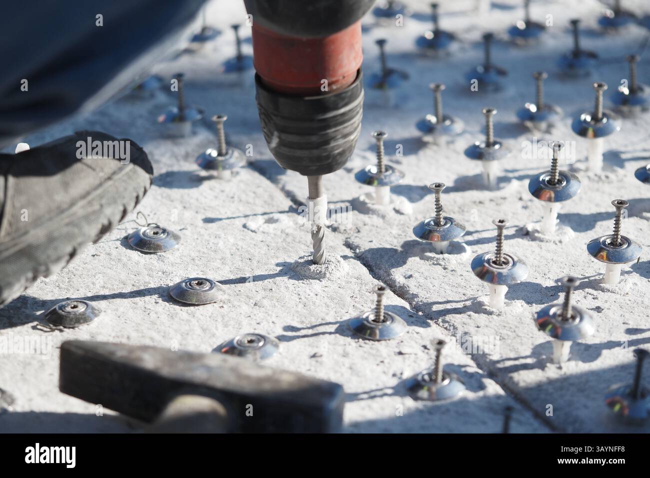 Construction worker drilling bolts into concrete surface at job site ...