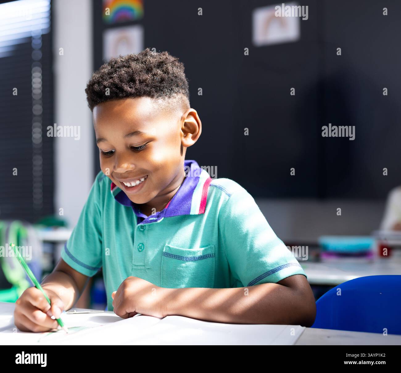 African American boy writing in notebook at school desk with green ...