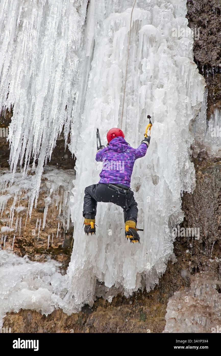 Man with ice axes and crampons climbing on icefall Stock Photo