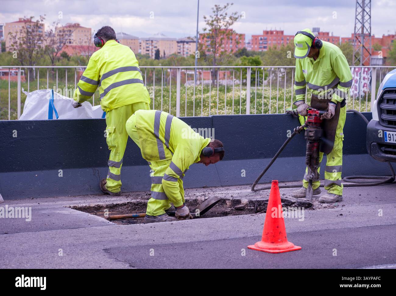 A construction worker in a yellow safety vest and hard hat is shoveling ...